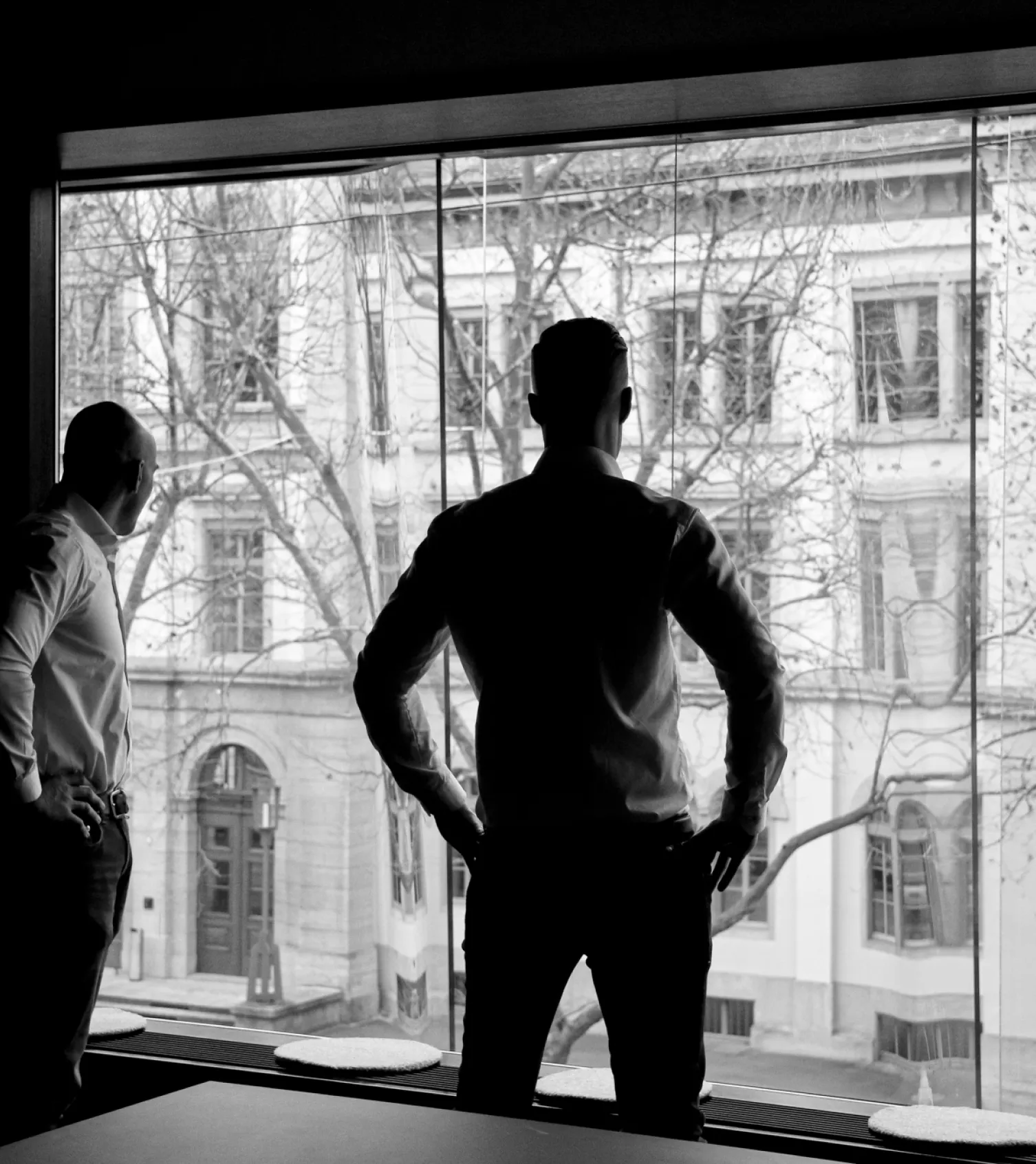 Schwarz-weiß-Bild von zwei Personen, die aus dem Fenster auf die Straße schauen, von hinten fotografiert