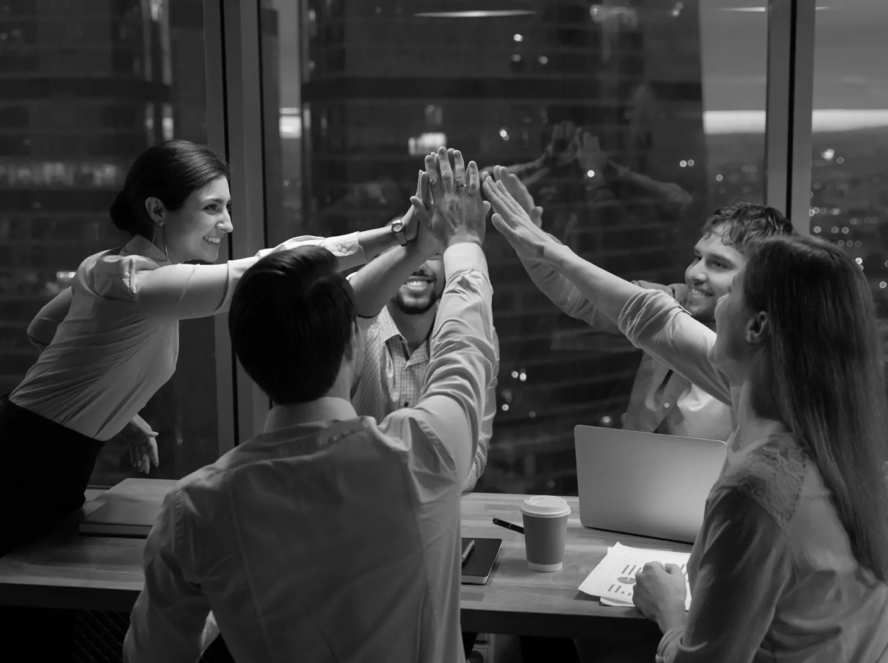 Schwarz-weiß-Bild: Fünf Personen an einem Besprechungstisch beim High-Five